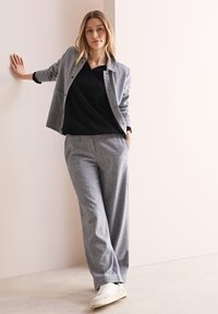 Grijs geruite blazer over een zwart top, gecombineerd met bijpassende grijze broek en witte sneakers. Soepele stoffen en een relaxte pasvorm.