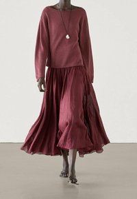 Maglione borgogna e una gonna maxi leggera e fluida a strati. Una semplice collana con ciondolo d'argento completa l'outfit.