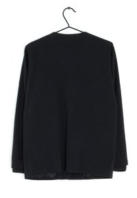 Black long-sleeve top with a textured fabric, loose fit, round neckline, and curved hem. Features ribbed cuffs and a hanging loop.