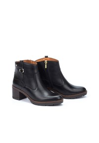 Bottines en cuir noir avec un bout rond, un talon bloc, un détail de fermeture éclair dorée sur le côté et une doublure intérieure beige. Semelle en caoutchouc texturé.