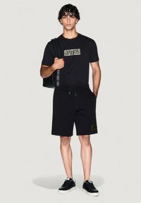 Outfit casual negro que presenta una camiseta de manga corta con un logo y pantalones cortos a juego. El material parece suave; los accesorios incluyen un bolso texturizado.