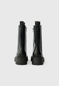 Crne kožne gležnjače s glatkom završnom obradom, visokim često, debelim crnim potplatima i stražnjim trakama za lakše oblačenje.