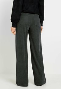 Pantalons en velours côtelé à jambes larges, de couleur gris foncé, avec des rayures verticales texturées, comportant deux poches arrière et une taille lisse.