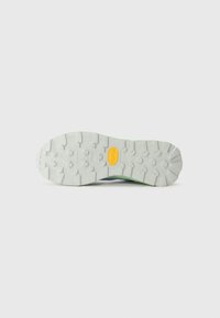 Suola di scarpa da trail con un design robusto e profondi intagli, realizzata in gomma grigia chiara, e un'igienica e prominente etichetta Vibram gialla per la trazione.