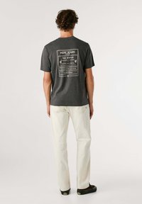Grijze katoenen T-shirt met een grafische print op de achterkant met tekst en randen. Gepaarde met off-white broeken en zwarte schoenen.