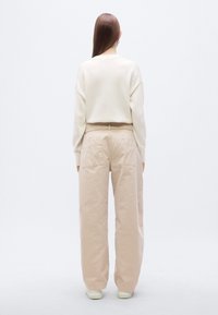 Κρεμ πουλόβερ με χαλαρούς ώμους, σε συνδυασμό με φαρδιές, ανοιχτό μπεζ παντελόνες με μεγάλες πίσω τσέπες και ελάχιστη υφή.