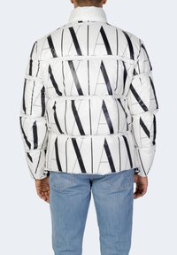 Giacca a vento bianca con strisce verticali nere e motivo testuale. Caratterizzata da un colletto alto e design trapuntato. Abbinata a jeans blu chiaro.