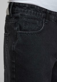 Svarte denimjeans med teksturert finish, med standard fem-lommers design og metallknapplukking. Subtile sømdetaljer synlige.