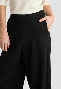 Zwarte wijde broek van soepele stof, met een hoge tailleband en zijzakken, en een strakke, minimalistische uitstraling.