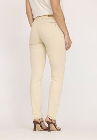 Jean skinny beige en denim, avec des poches arrière, une texture lisse et une coupe ajustée, associés à des escarpins bruns à lanières.