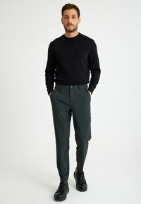 Zwarte lange mouw shirt, grijs geruite broek en zwarte sneakers; gemêleerde stof en op maat gemaakt met een klassiek ontwerp.
