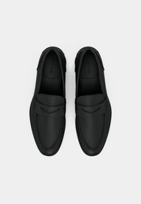 Mocassins noirs en matériau semblable au cuir lisse, présentant un design cousu, un bout légèrement pointu et une bande décorative simple à travers le coup de pied.