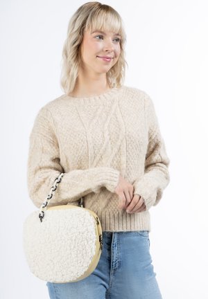 Beżowy sweter dzianinowy z wzorem w warkocze, połączony z okrągłą torbą w białym kolorze o teksturze futra, z żółtą ramką i srebrnym łańcuszkiem.