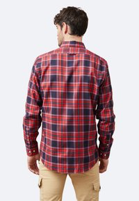 Camisa de hombre de manga larga en patrón de cuadros rojos, azules y negros. Cuenta con un cuello abotonado y un dobladillo curvado. Tela de algodón, textura suave.