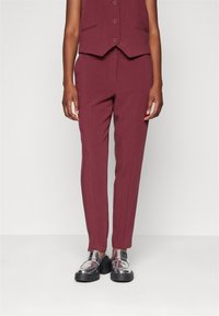 Mörkröd skräddarsydd väst med knappstängning och två sido fickor, tillsammans med smalpassande mörkröda byxor. Tillbehör inkluderar blanka silverfärgade mockasiner.