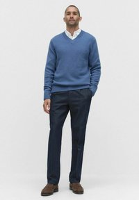 Niebieski sweter dzianinowy z dekoltem w serek, w zestawieniu z ciemnymi, dopasowanymi spodniami i brązowymi butami. Stylizacja cechuje się gładką teksturą, prostymi liniami i minimalistycznym designem.