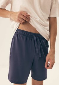 Granatowe szorty z elastycznym paskiem i sznurkiem, wykonane z lekkiego materiału. W połączeniu z białą koszulką, odsłaniającą okolice talii.