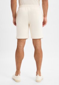 Crèmekleurige korte broek gemaakt van zachte stof, met een elastische tailleband en zijzakken. De zoom is licht opgerold.