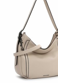 Sac à main en cuir beige texturé avec des accents noirs, muni d'une seule bandoulière et d'un petit charme décoratif attaché.