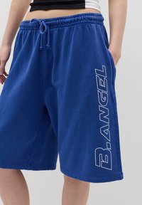 Blue cotton shorts with an elastic waistband and drawstring. Features side pockets and white "B.Angel" text printed on the leg.