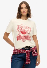 Kremowy T-shirt z krótkim rękawem z czerwonym graficznym motywem góry, drzew i kwiatów. Casualowy krój, zestawiony z ciemnymi dżinsami i koszulą w kratę zawiązaną w pasie.