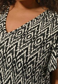 Black and white patterned top featuring a V-neck design, short sleeves, geometric shapes, and a soft fabric texture.