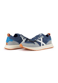 Sneaker atletiche blu e grigie realizzate in materiale mesh e suede, con accenti bianchi, una linguetta posteriore arancione e suola arancione.