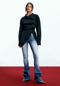 Top asimetric negru cu guler lat, asortat cu blugi deschiși la culoare, evazați, cu tivuri volănaș și pantofi cu toc ascuțit negri.