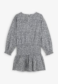 Vestido de patrón en blanco y negro con mangas largas, cintura fruncida, dobladillo de peplum y cierre en la espalda con forma de llave. La tela tiene una apariencia suave y texturizada.