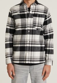 Zwart-wit geblokte flanellen shirt met knoopsluiting, kraag en borstzak; gestructureerde stof met variërende patroonformaten.