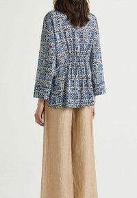 Top blu con motivo floreale, maniche lunghe e dettagli arricciati sul retro, abbinato a pantaloni beige a gamba larga in un tessuto testurizzato.