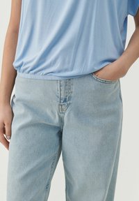 Lysblå kortærmet top med en samlet kant, parret med lysblå denim jeans med klassisk pasform og frontlommer.