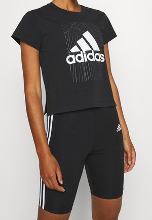 Personne portant un t-shirt Adidas noir avec un logo blanc et un short taille haute noir avec des bandes blanches sur les côtés et un petit logo Adidas.