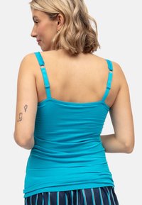 Turquoise tanktop met verstelbare spaghettibandjes, aansluitend ontwerp, geribbelde textuur en een gladde afwerking. Huid zichtbaar op de rug.