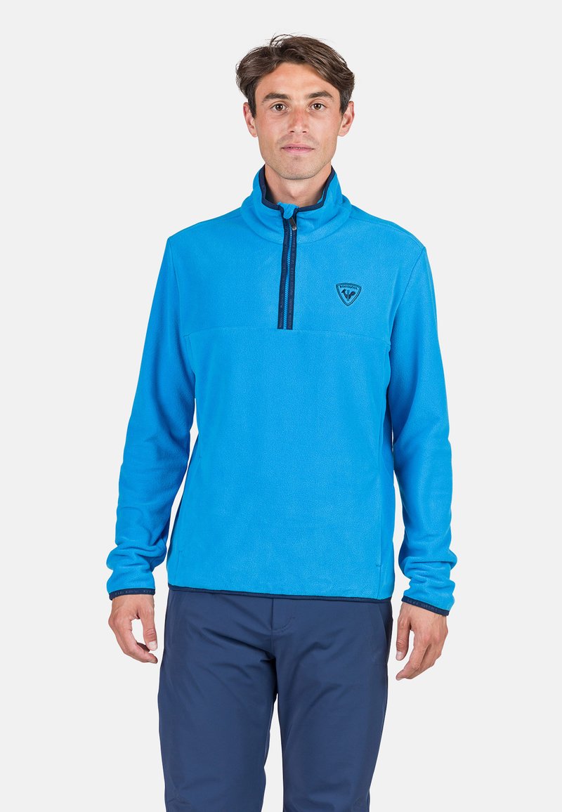 Pullover in pile azzurro chiaro con alto colletto, zip frontale a metà e logo sul petto. Maniche lunghe con polsini elasticizzati. Tessuto morbido.