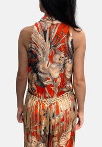 Top senza maniche rosso con motivi floreali e foglie beige e nere. Presenta una cintura decorativa frangiata in vita. Tessuto liscio e leggero.