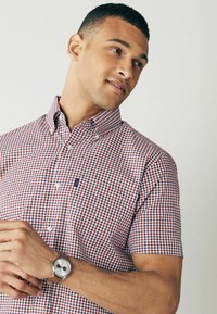 Korte ærmer button-down skjorte i et rødt, hvidt og blåt ternet mønster med et logo på brystlommen og en spidse krave.