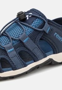 Jūras zils sporta čību modelis ar elpojošu sietu augšdaļu, elastīgu ātru saistīšanas sistēmu un izturīgu gumijas zoli ar strukturētu virsmu.