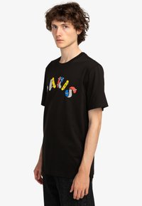 Černé bavlněné tričko s barevným grafickým textovým designem se skateboardy. Kulatý výstřih a krátké rukávy, volný střih, jednoduchá textura.