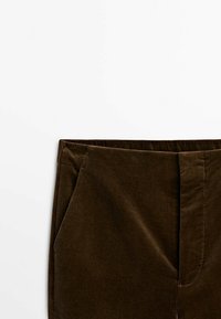 Pantalons en velours côtelé marron avec une surface texturée, des poches latérales et une taille ajustée. Aucune motif visible ni détails en matériel.
