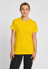 Geel katoenen t-shirt met korte mouwen, ronde hals en een gladde textuur, gecombineerd met zwarte aansluitende leggings.
