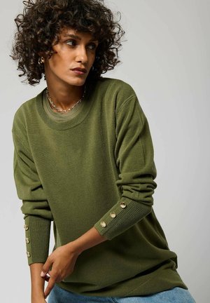 Pull en vert olive avec un col rond, des poignets côtelés ornés de boutons dorés et une coupe décontractée. Texture douce, design casual.