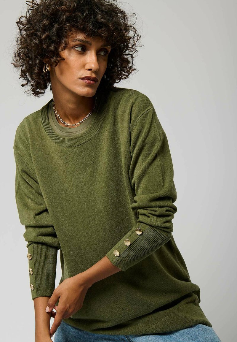 Maglione verde oliva con scollatura rotonda, polsini a coste con bottoni dorati e vestibilità morbida. Texture soffice, design casual.
