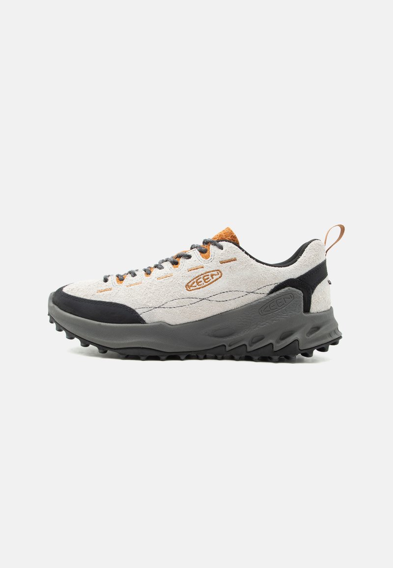Chaussure de randonnée gris clair et noir avec semelle robuste, accents orange, fermeture à lacets à l'avant et languette au talon sur fond blanc.