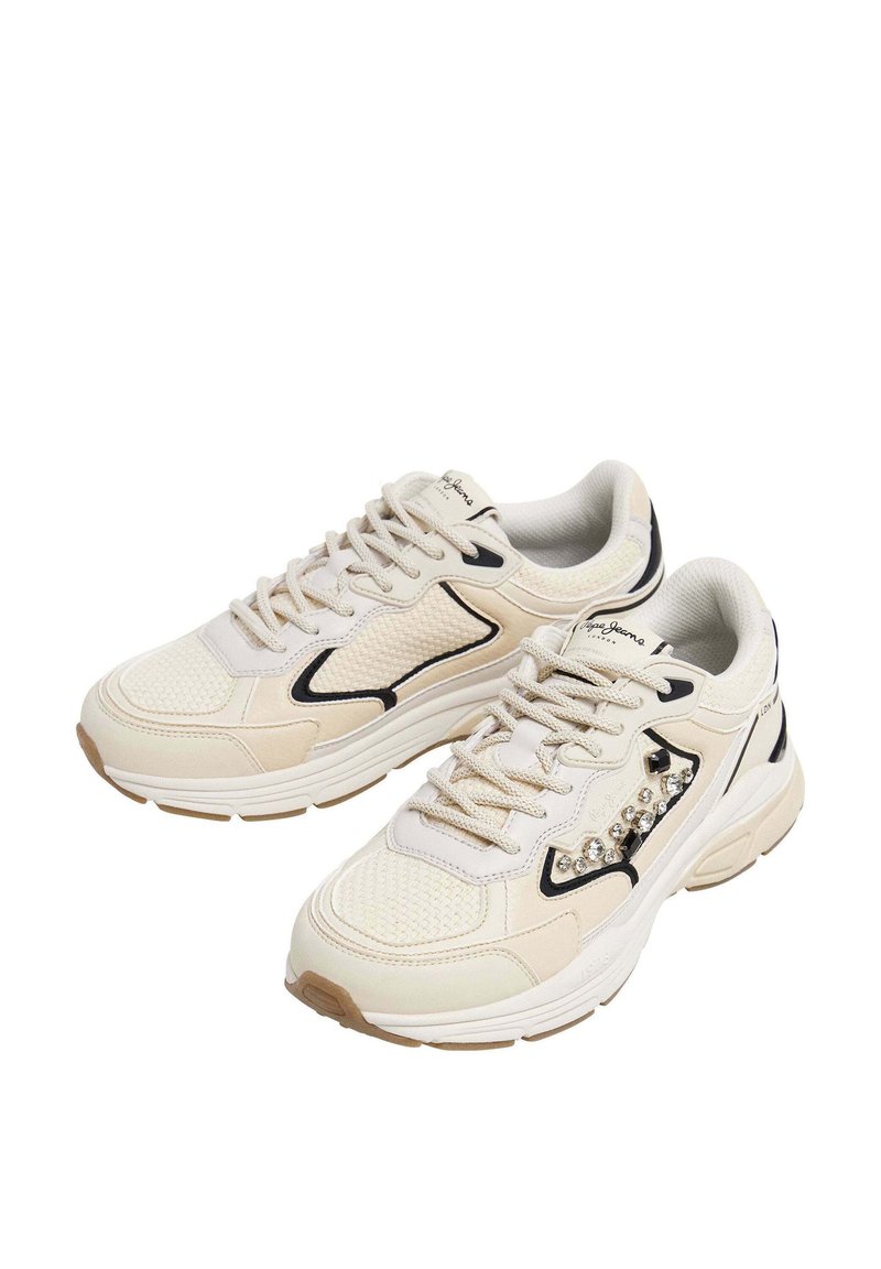 Sneaker in rete crema e beige con dettagli neri. Presentano cristalli decorativi sul lato, pannelli testurizzati e una suola robusta.