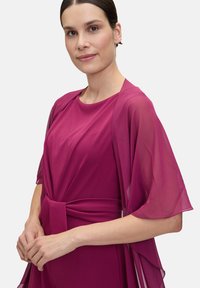 Fuchsia dress with a flowing, sheer cape, round neckline, and a knotted waist tie. Smooth fabric texture with draped sleeves.