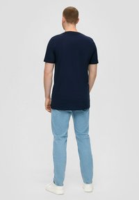 Marineblauwe katoenen T-shirt met korte mouwen en een klassieke ronde hals, gedragen met lichtblauwe jeans en witte sneakers.