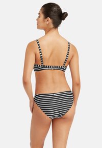 Czarny i biały kostium kąpielowy w paski z regulowanymi ramiączkami i zapięciem na haczyk z tyłu. Miękka, elastyczna tkanina z umiarkowanym zakryciem.