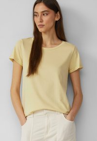 Lichtgeel T-shirt met korte mouwen, gemaakt van zachte katoen. Heeft een ronde halslijn en opgerolde mouwen, gecombineerd met lichte broek.