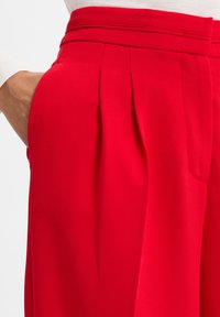 Rote plissierte Hose mit strukturiertem Bund, Seitentaschen und einem strukturierten Stoff, der vertikale Rippung zeigt.